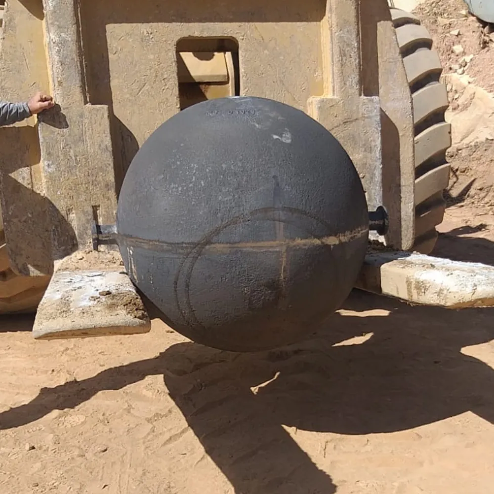 Esfera metálica DropBall ao lado de escavadeira em operação de fragmentação de rochas em campo