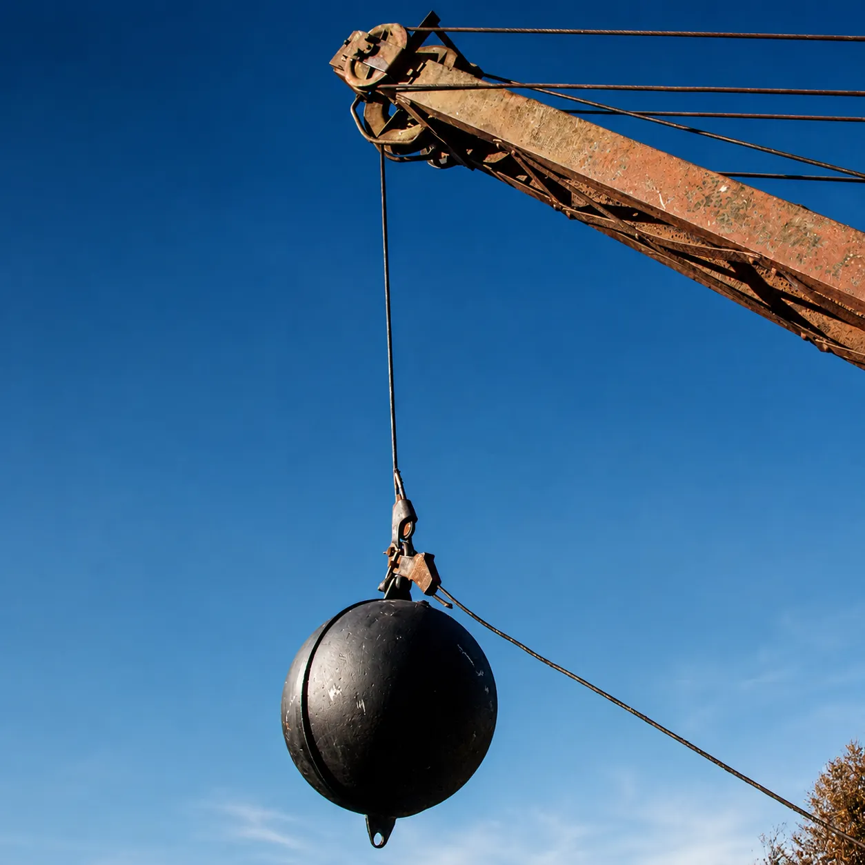 Esfera metálica DropBall içada por guindaste contra o céu, pronta para operação de demolição por impacto